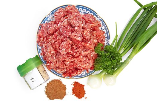 Minced meat on a plate with onions and spices isolated on white background