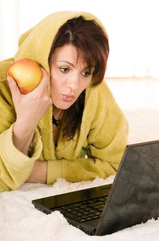 Woman in robe with laptop and apple lying on the floor