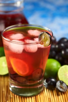 Refreshing homemade red grape lemonade made of red grape and lime juice chilled with ice cubes (Selective Focus, Focus on the front rim of the glass and the front of the grape slice garnishing the rim)