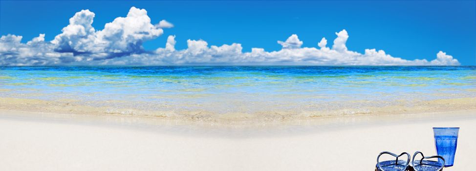 Tropical beach with beach shoes and blue glass of water