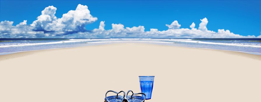Tropical beach with beach shoes and blue glass of water