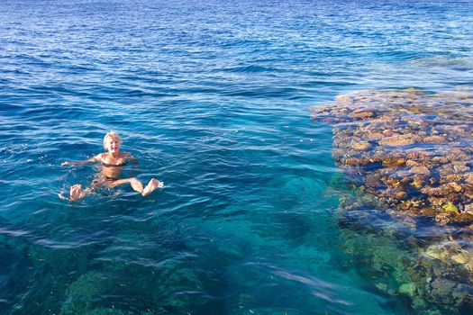 The girl carefree swim in the sea near to corals, pleasure by the sea