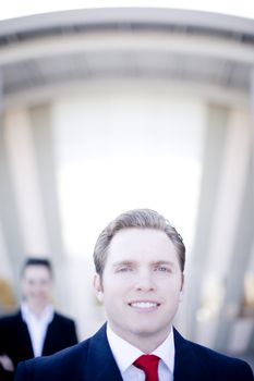 attractive young businessman with businesswoman in background standing in front of building