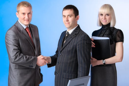 Business team of three people, two men shaking hands.