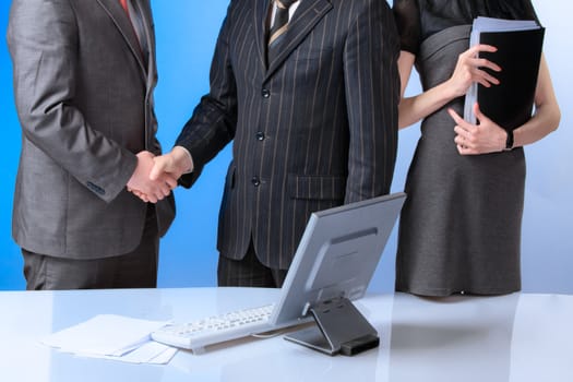 Business team of three people, two men shaking hands.