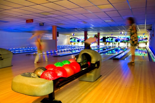 Silhouettes of people active bowling in dark bowling hall with colorful flashing disco lights