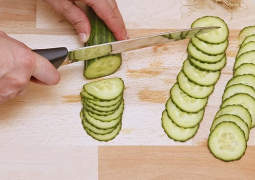 Upper view of hands with a knife chopping a cucumber.