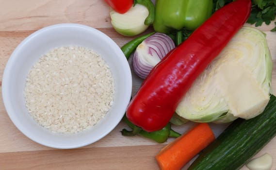Upper view of a bowl of rice near fresh vegetables on a choping board.