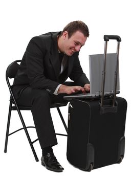 Young smiling man traveler working in a hurry on his latop on a suitcase- isolated against a white background.