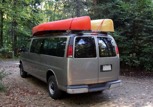 A large van with a canoe on top, shot against the early fall forest.
