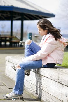 Preteen girl tying shoes outdoors near lake