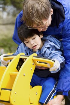 Father helping disabled son play on playground equipment