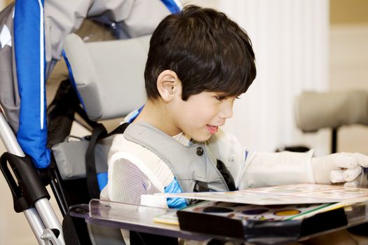 Disabled four year old boy studying or reading in wheelchair