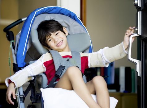 Handsome four year old disabled boy in wheelchair opening front door, smiling a welcome