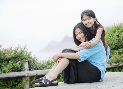 Two beautiful sisters sitting together near a misty ocean in the background