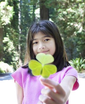 Ten year old Asian girl holding out large three leaf clover