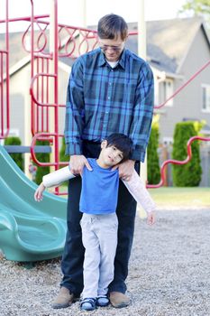 Father helping disabled four year old son to play at playground