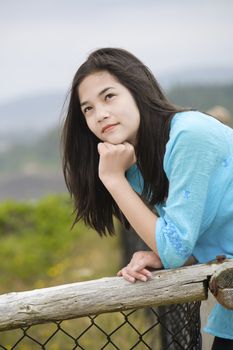 Preteen biracial girl by ocean shore with a thoughtful look, looking up