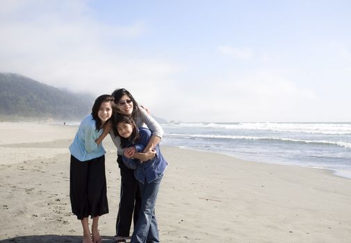 Asian mother and two daughters smiling on the beach by ocean.