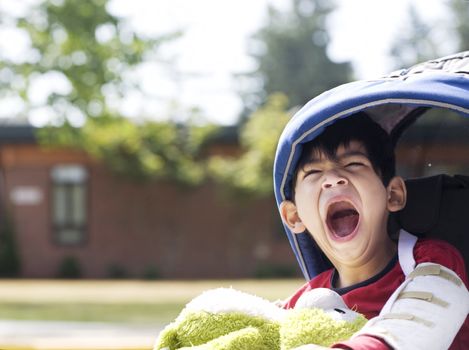 Disabled five year old boy in wheelchair in front of school, yawning