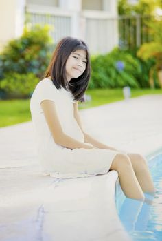 Ten year old girl repaxing by swimming pool, smiling