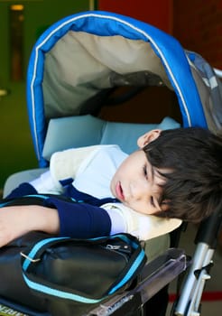 Disabled five year old boy in wheelchair at school, looking tired