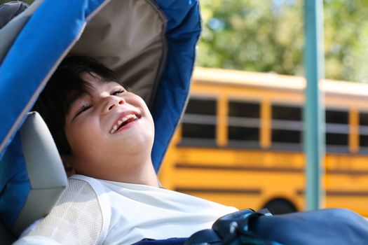 Disabled five year old boy in wheelchair outdoors by school bus