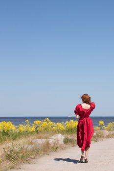 Young lady near the sea in long red dress. Near beauty yellow flowers