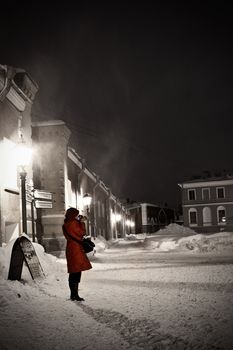 Lady takes a picture at the night. She is in red coat and red hat