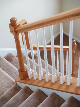 A view down a stairway in a modern american home. Carpeted stairs and a wooden banister and railing are visible