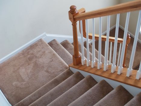 A view down a stairway in a modern american home. Carpeted stairs and a wooden banister and railing are visible