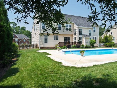 A modern luxurious American home and backyard with a lush lawn, inviting swimming pool and deck with chairs.