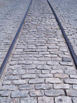 Train tracks embedded in down the middle of an old cobblestone road.