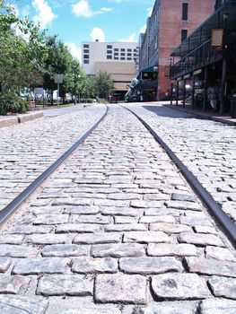 Metal train tracks embedded in a cobblestone road in front of old buildings along a waterfront