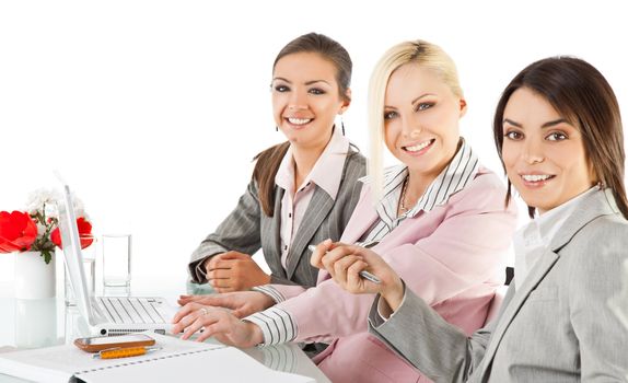 Group of three happy businesswomen working behind desk with laptop, looking at camera