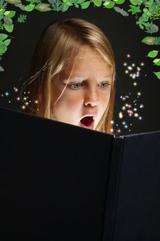 Pretty young school girl engrossed in reading a book with stars coming out of it
