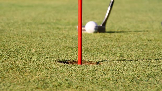 A club is hitting a golf ball on the green