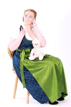 Woman in traditional Bavarian dress during phone calls with a teddy bear on her lap