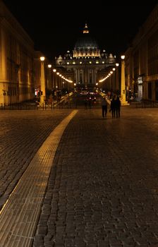 A stone path in Rome, with St. Peter's Basilica in the background, in Vatican city at night.
