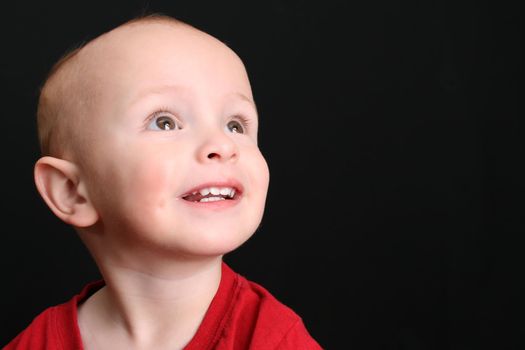 Blonde toddler against a black background looking up