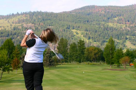 Blond female golfer following her shot from the tee-box down the fairway 
