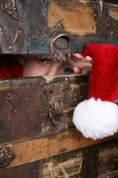 Serious boy with a christmas hat peeping from inside an antique trunk