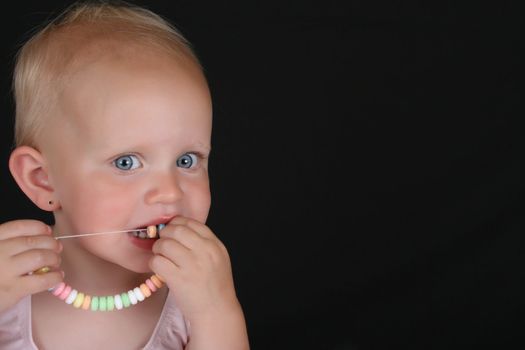 Cute blond toddler eating a candy necklace