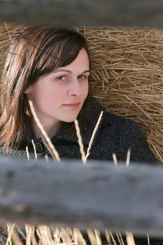Beautiful brunette female leaning against hay bales