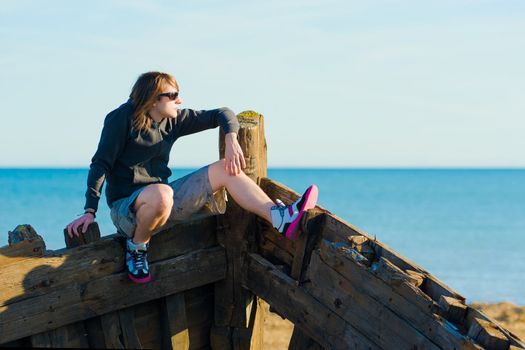 Teenager sitting on the prow of a shipwreck, a concept