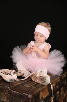 Blond toddler wearing a tutu holding Ballet shoes 