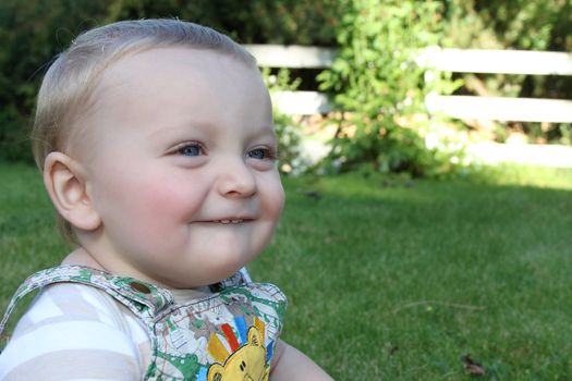 Cute blond baby boy sitting outside in the garden