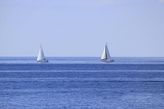 Two sailboats on open blue sea horizon