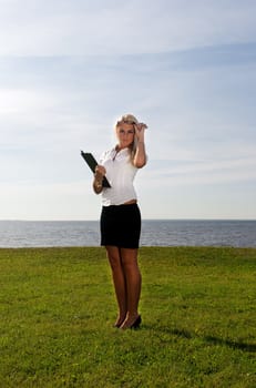 girl in glasses standing with a folder on the background of the sea, sky and grass