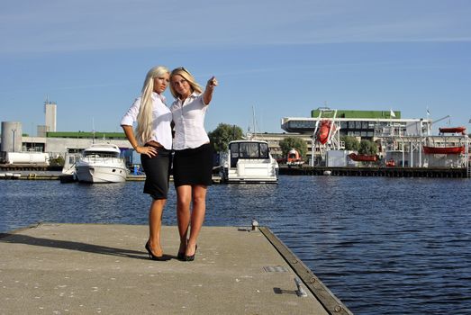 Two girls blonde stand on the pier and point a finger